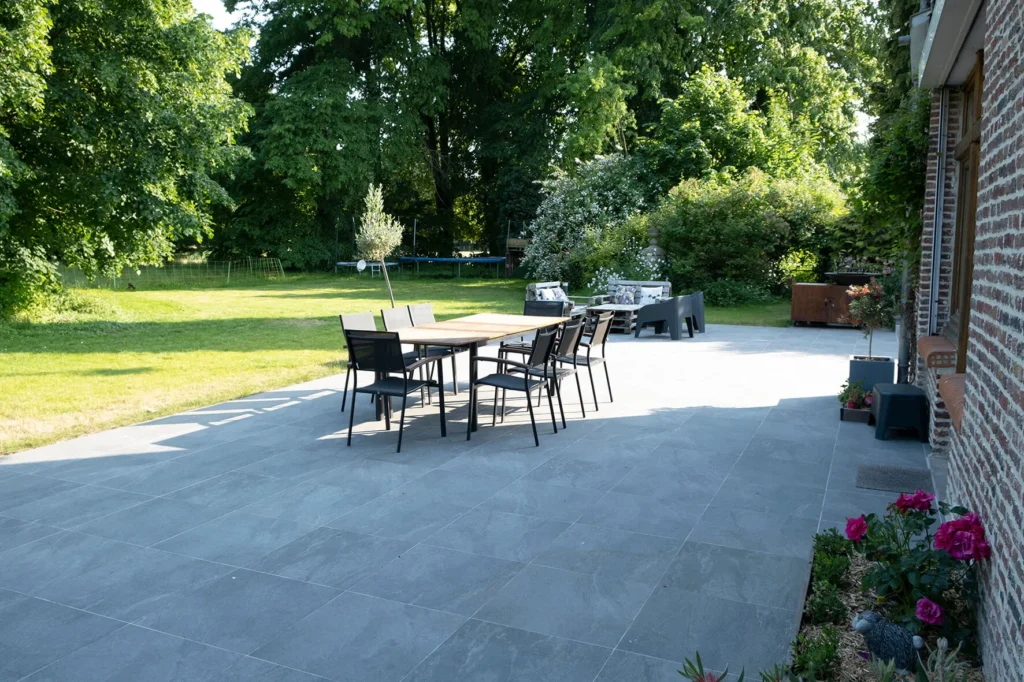 Terrasse en grès ceram qui donne sur un jardin boisé avec une décoration extérieure en fer forgé